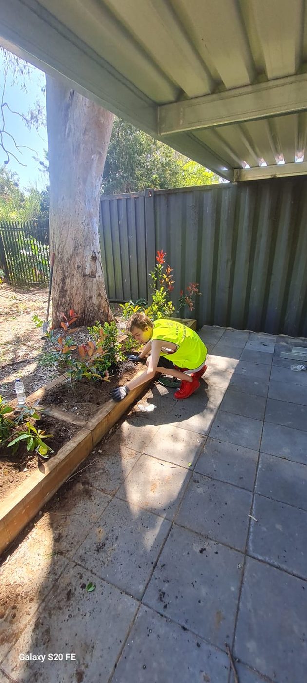 A participant in a hi-vis vest planting garden beds as part of landscaping training
